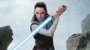 Dais Ridley's Rey holds her blue lightsaber facing downward. Rey will return to Star Wars in one of three new movies.