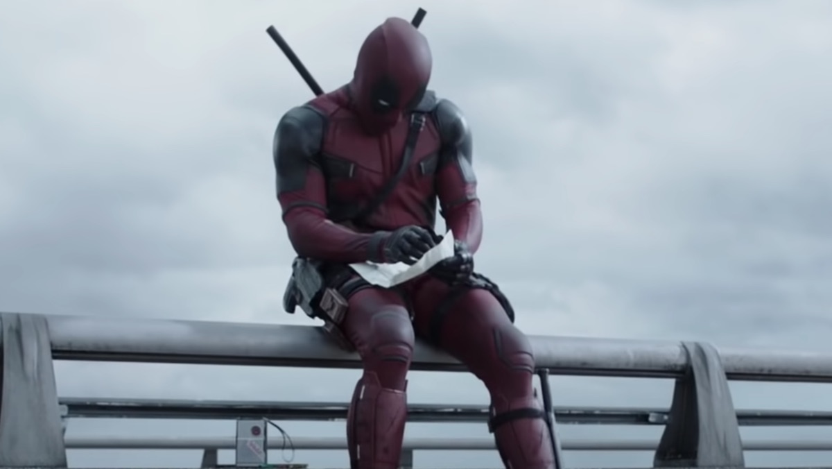Deadpool sitting near a highway drawing on a piece of paper