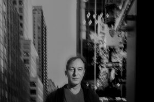 A black-and-white photo of a man on a street in New York City, tall buildings behind him.