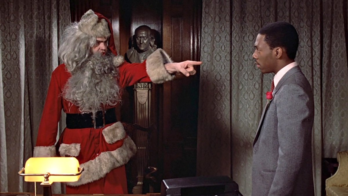 Dan Aykroyd dressed in a dity Santa suit points at Eddie Murphy in Trading Places