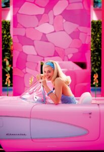 A woman in a headband smiles and waves from a bright pink convertible in "Barbie."