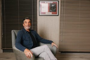 Chuck Lorre in a denim jacket and light gray pants sits in a chair at his office on the Warner Bros. lot.