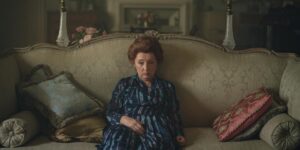Lesley Manville as Princess Margaret sitting on a couch in a blue and black striped dress.