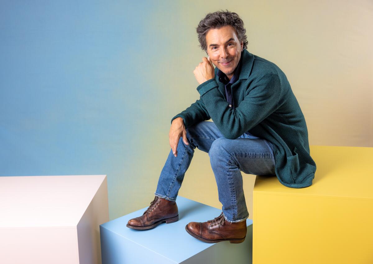 Director Shawn Levy poses for a portrait sitting on a large cube while resting his feet on a smaller one.
