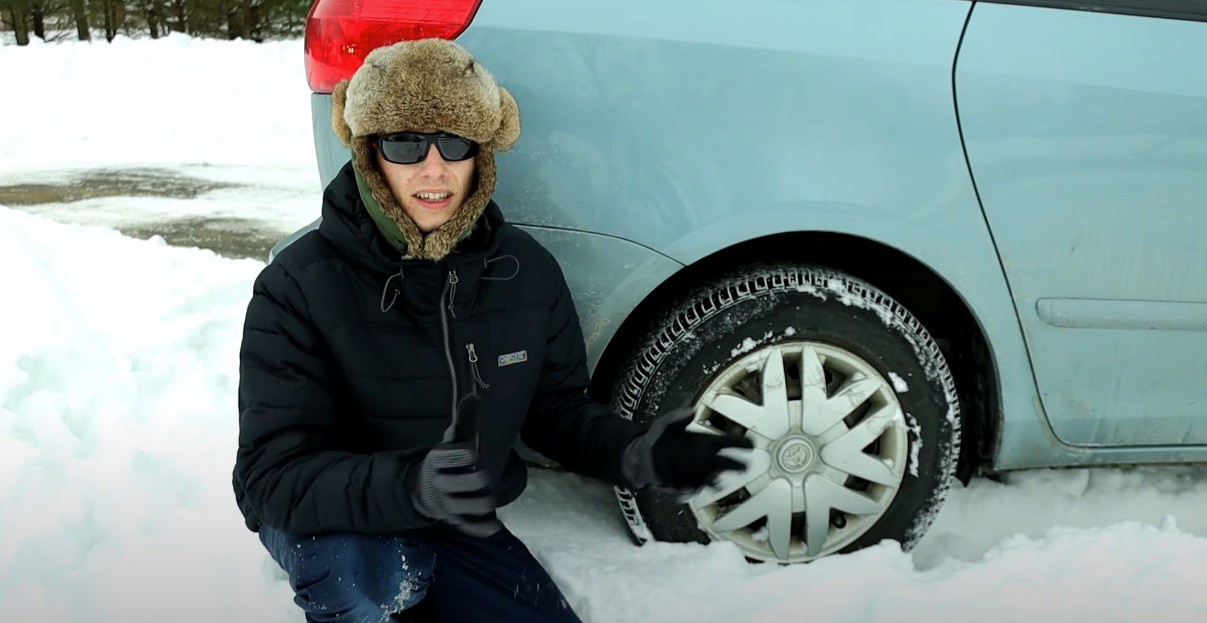 The video featured the YouTuber all bundled up in layered clothing in winter snow, kneeling behind the back tire of a vehicle
