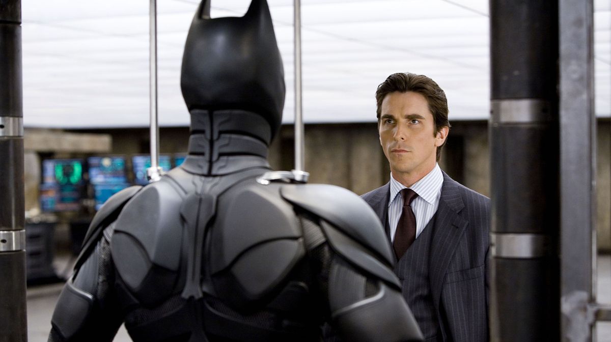 Bruce Wayne (Christian Bale) grimly stands across from the Batman suit in The Dark Knight