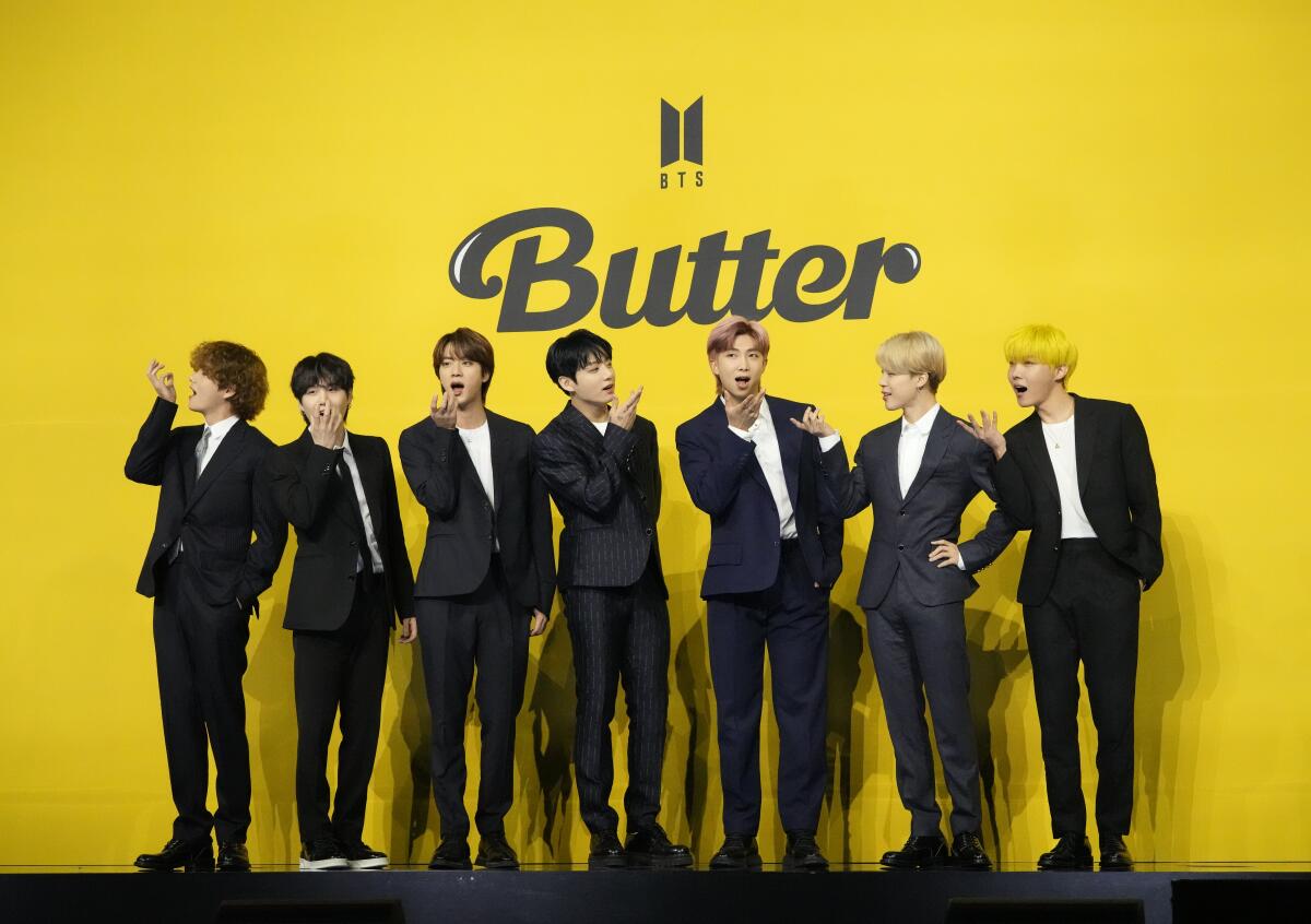 Seven men in dark suits posing against a yellow background