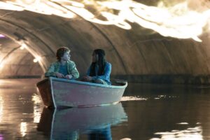 Percy (Walker Scobell) and Annabeth (Leah Sava Jeffries) sitting in a boat in a tunnel