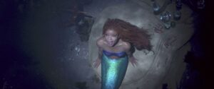 Halle Bailey with Ariel’s green fin and red hair singing while looking up from the bottom of the ocean in The Little Mermaid