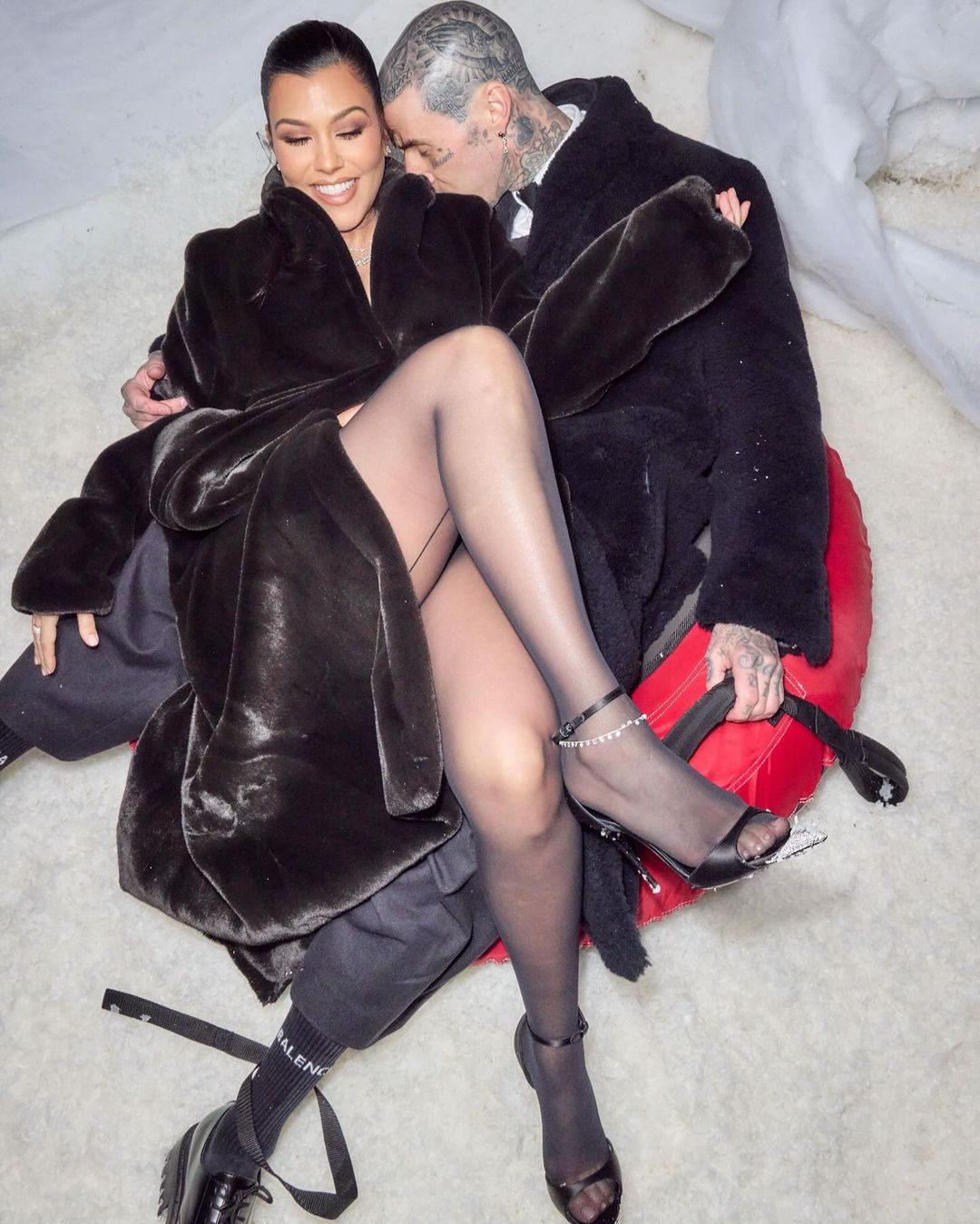 Kourtney, pictured with her husband Travis Barker, wore an oversized fur-like coat with a black bodysuit and semi-sheer black tights underneath for the party