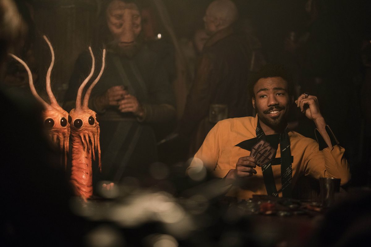 Donald Glover as Lando Calrissian in Solo: A Star Wars story. He lounges smarmily at a sabacc gambling table, surrounded by weird aliens. 