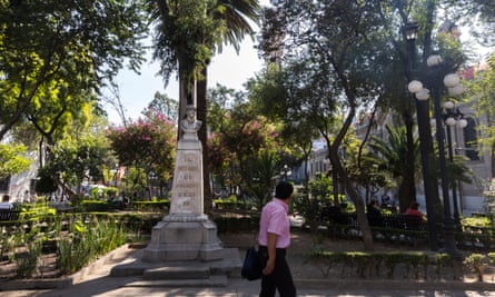 A man in a short-sleeved shirt walks by the bust of businessman Ernesto Pugibet with palm trees behind it