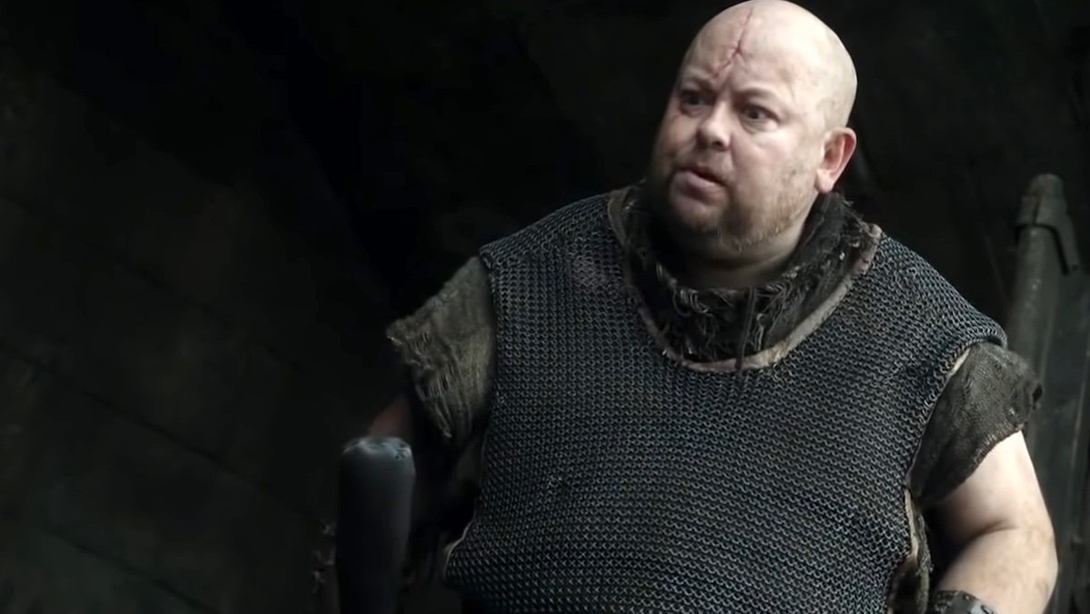 Mord the Jailer, a bald man in black with a big head scar holding a club on Game of Thrones