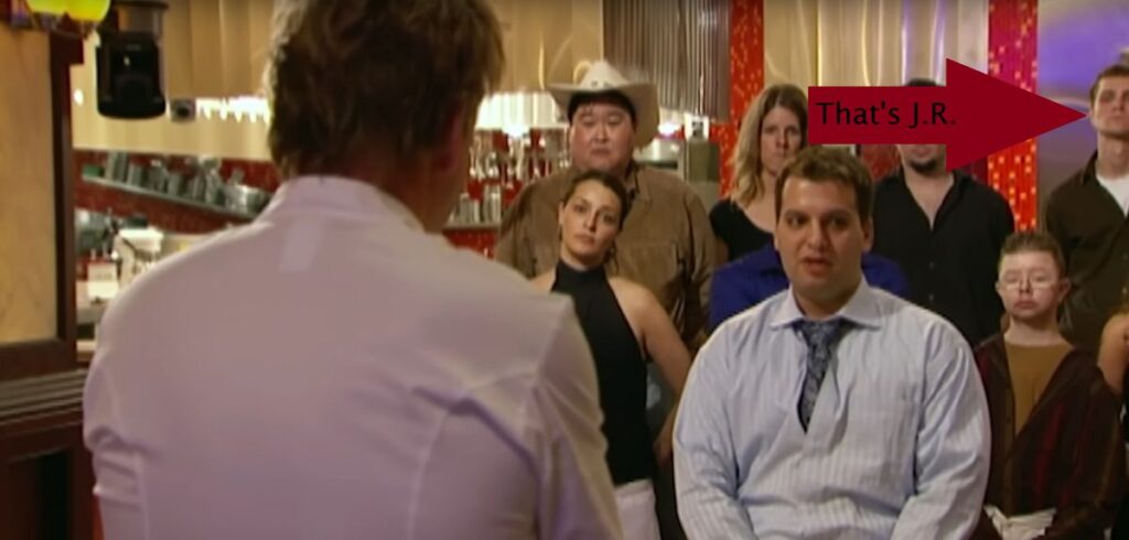 Gordan Ramsay has his back to the screen while a chef stands in front of him presenting a dish