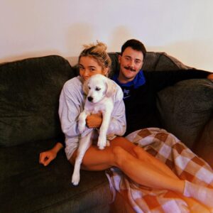 Olivia Dunne and Paul Skenes cozying up together on a couch with their puppy Roux.