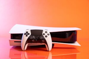 A Sony DualSense Edge controller resting on a PlayStation 5 with an orange background.