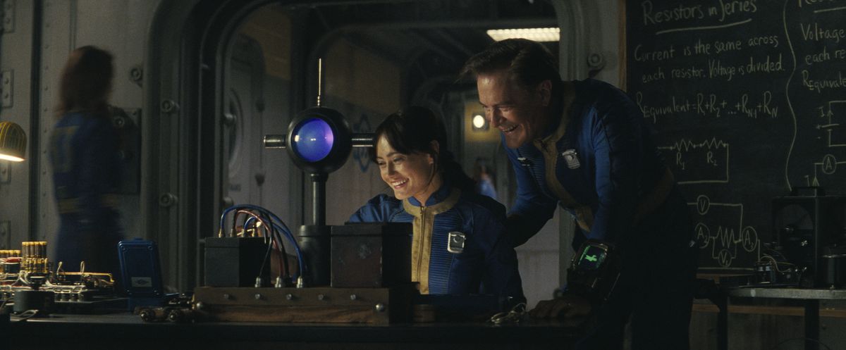 Lucy (Ella Purnell) and Hank (Kyle MacLachlan) sitting in front of a gadget and laughing in a still from the Fallout TV series