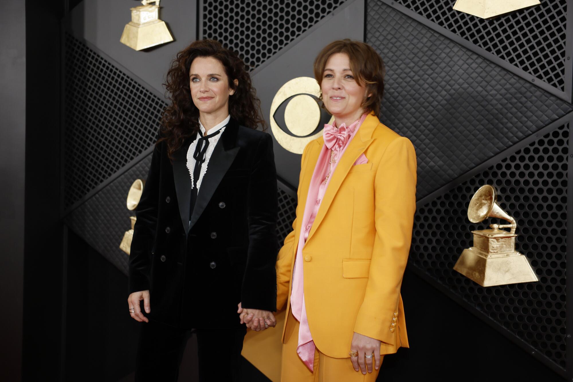 A woman in a black suite holds hands with a woman in a yellow suit
