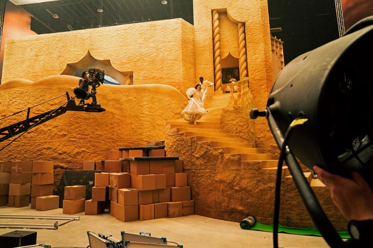 A film set shows two people running down golden-tinted stairs while a camera on a crane gets the shot.