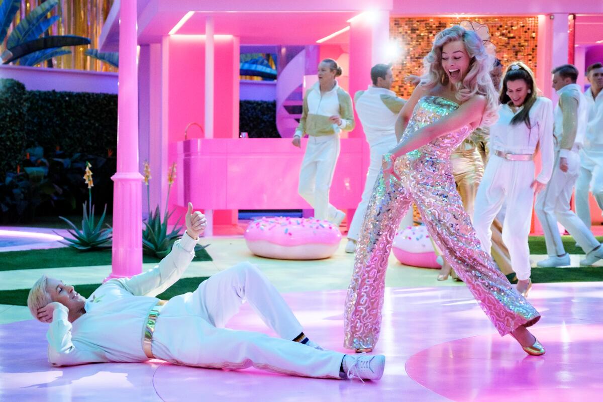 A man dressed all in white lies on a dance floor as a woman in sparkly silver dances around him in "Barbie."