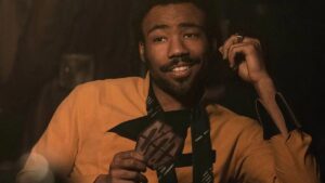 Donald GLover smirks in his yellow shirt playing cards as Lando Calrissian