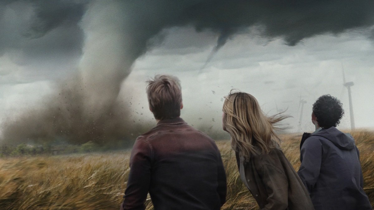 Three people seen from behind watching tornadoes in a poster for Twisters