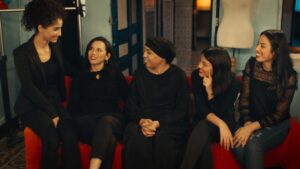 Five women sit on a red couch.