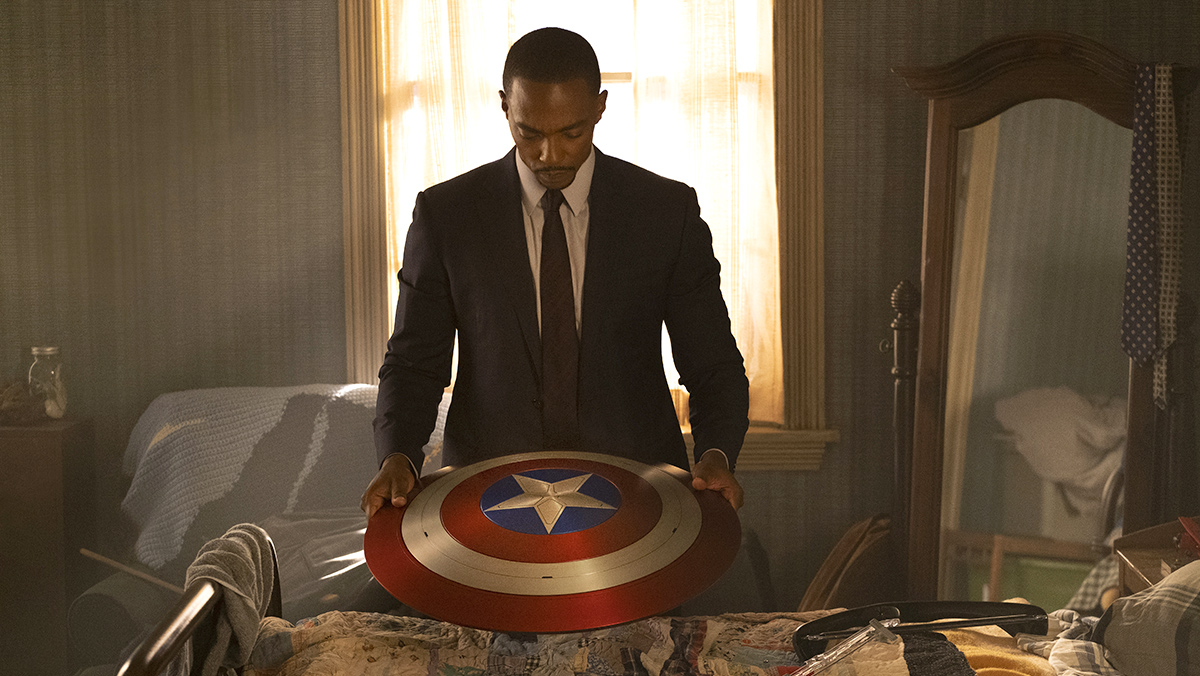 Sam Wilson stands holding the shield of Captain America looking somber in The Falcon and the Winter Soldier