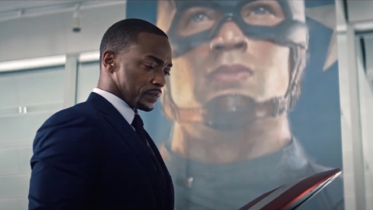 Sam Wilson (Anthony Mackie) somberly stands in front of a banner of Captain America in The Falcon and The Winter Soldier.