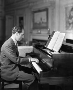A black and white photo shows a man playing a piano.