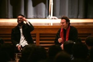 Two men talk in front of a crowd.