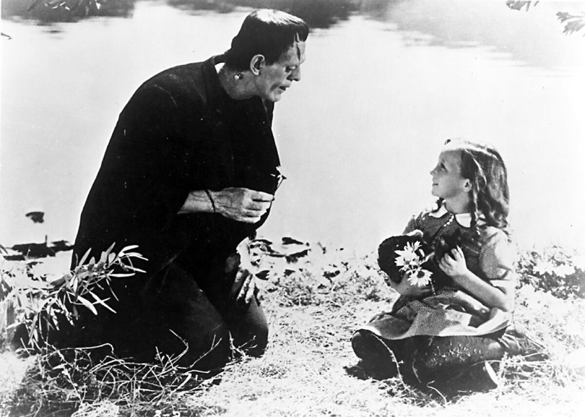 Frankenstein kneels down to sit with a little girl in the black and white 1931 "Frankenstein." 