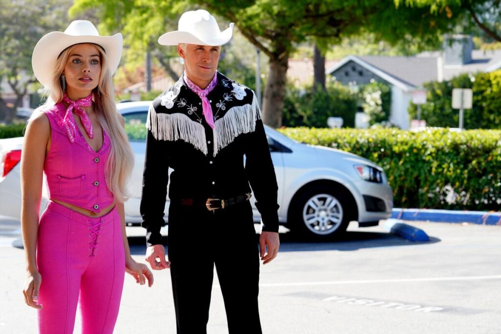 Barbie in a pink jumpsuit and cowboy hat and Ken, in a black and white fringed cowboy shirt, visit L.A. in "Barbie."
