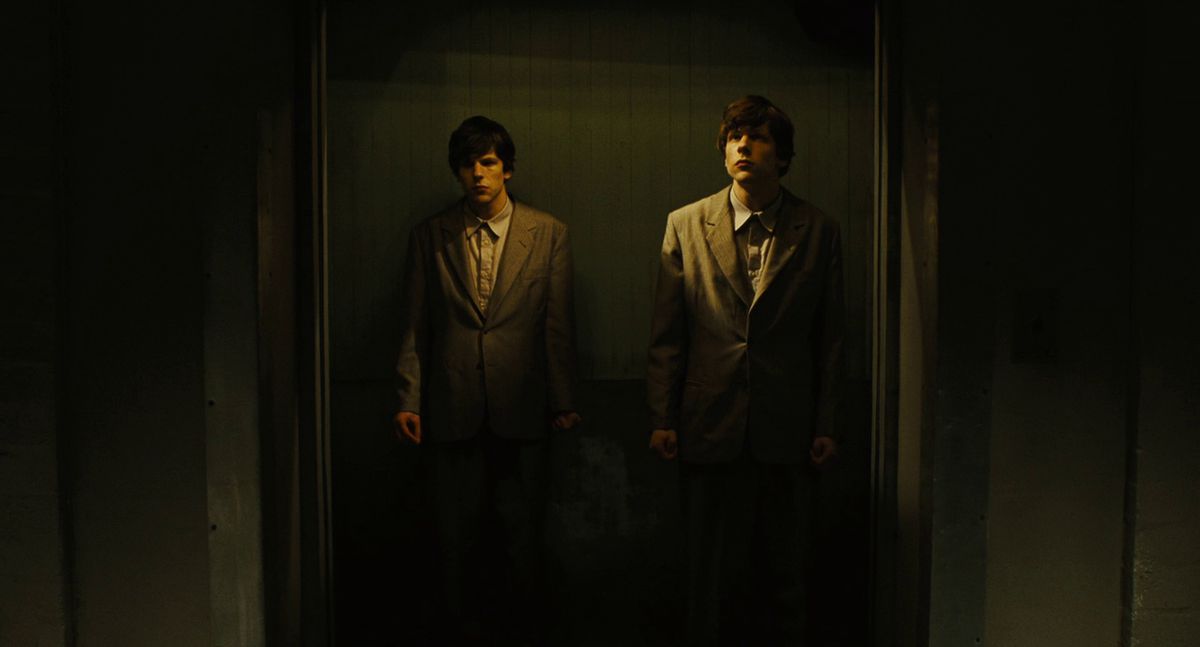 Two Jesses Eisenberg stand together in an elevator in The Double
