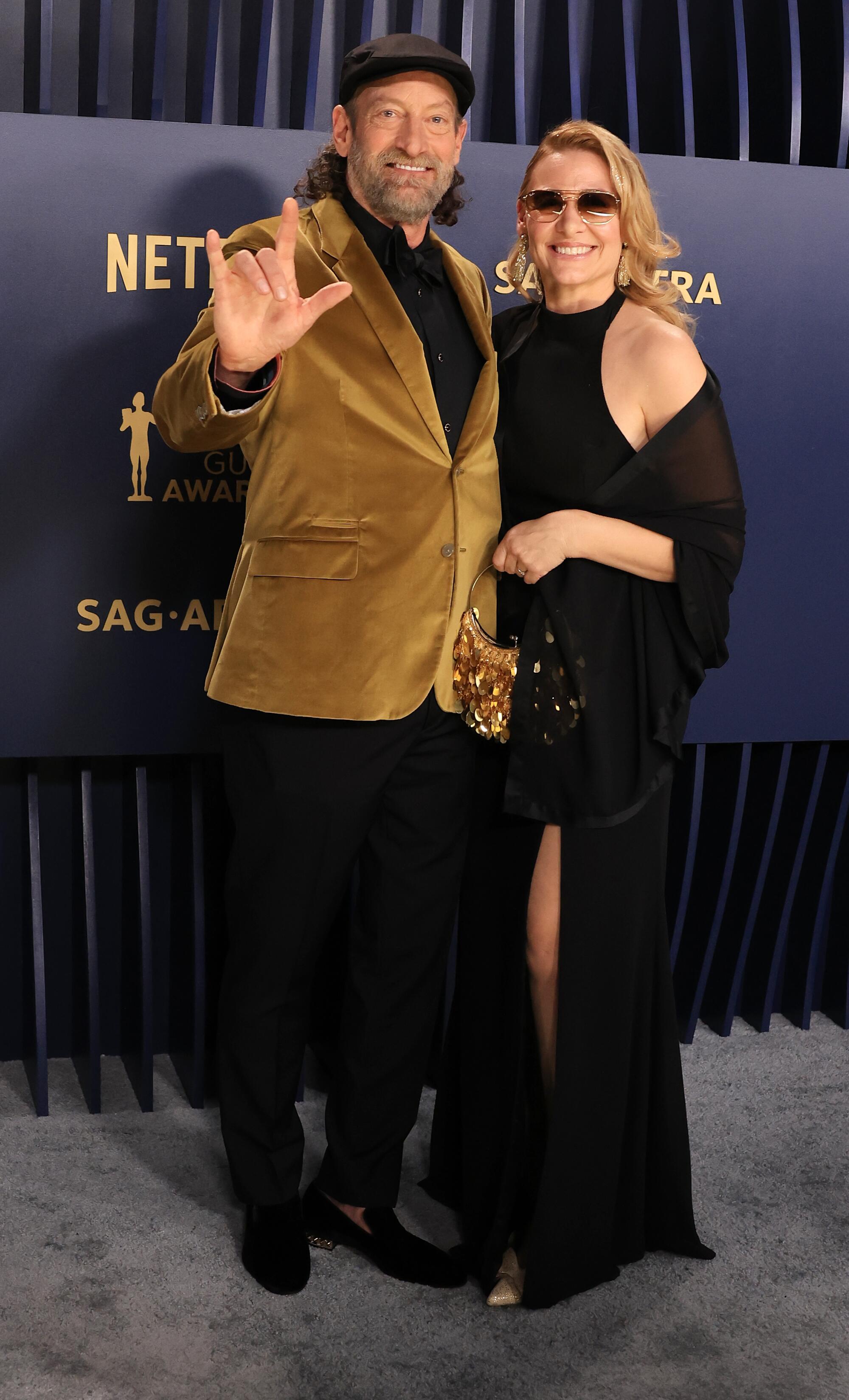 Troy Kotsur wears a gold velvet suit jacket and Deanne Bray wears a black dress at the SAG Awards.