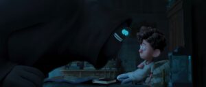 A little boy cowering in bed while a smiling and goofy looking dark figure stands over him