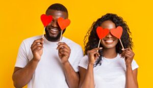 Cheerful black couple covering eyes with red heart paper cards - stock photo