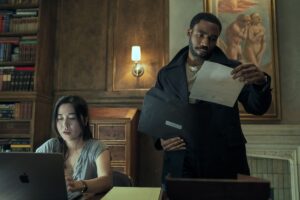Maya Erskine looks at a laptop while Donald Glover studies a document in a fancy study in Mr. &amp; Mrs. Smith