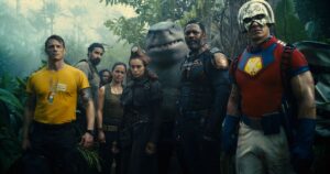 (L-R) Joel Kinnaman, Alice Braga, Daniela Melchior, Idris Elba, and John Cena standing in a tropical forest clearing in The Suicide Squad.