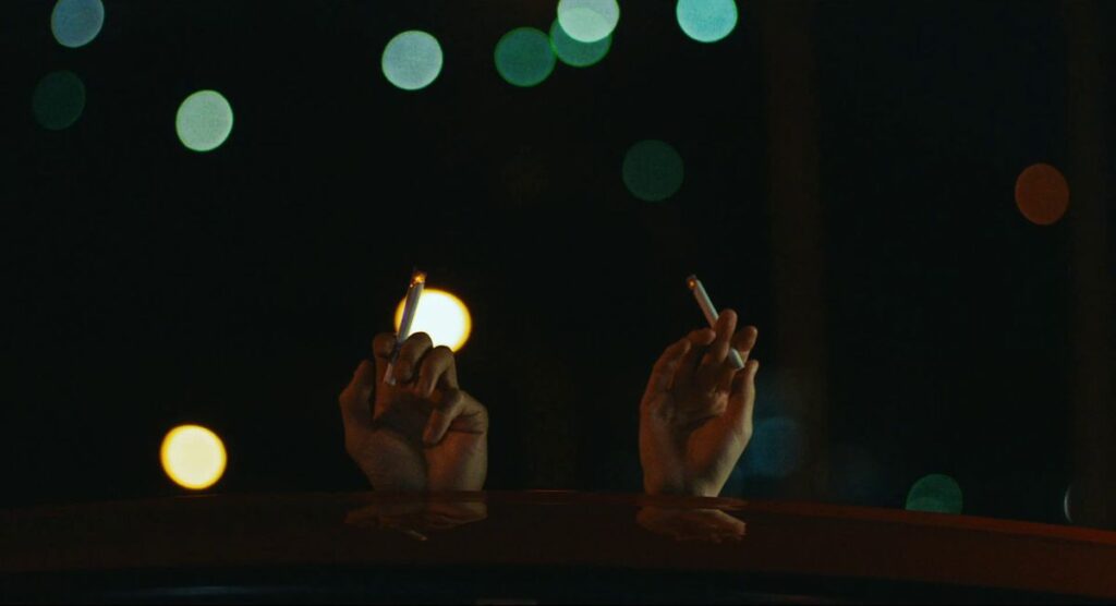 Two hands on the roof of a car holding cigarettes against the night sky.