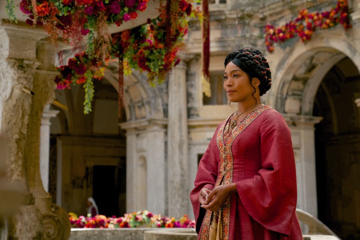 Angela Bassett in a red regal medieval fantasy-style gown, standing in a garden courtyard