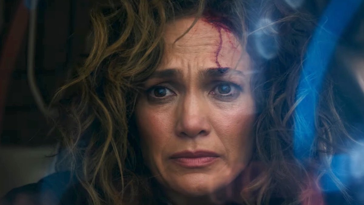 A bloodied Jennifer Lopez looks worried behind 3D computer images in Atlas from Netflix