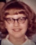 An old photo of a young woman with 60s-style glasses and hairdo.