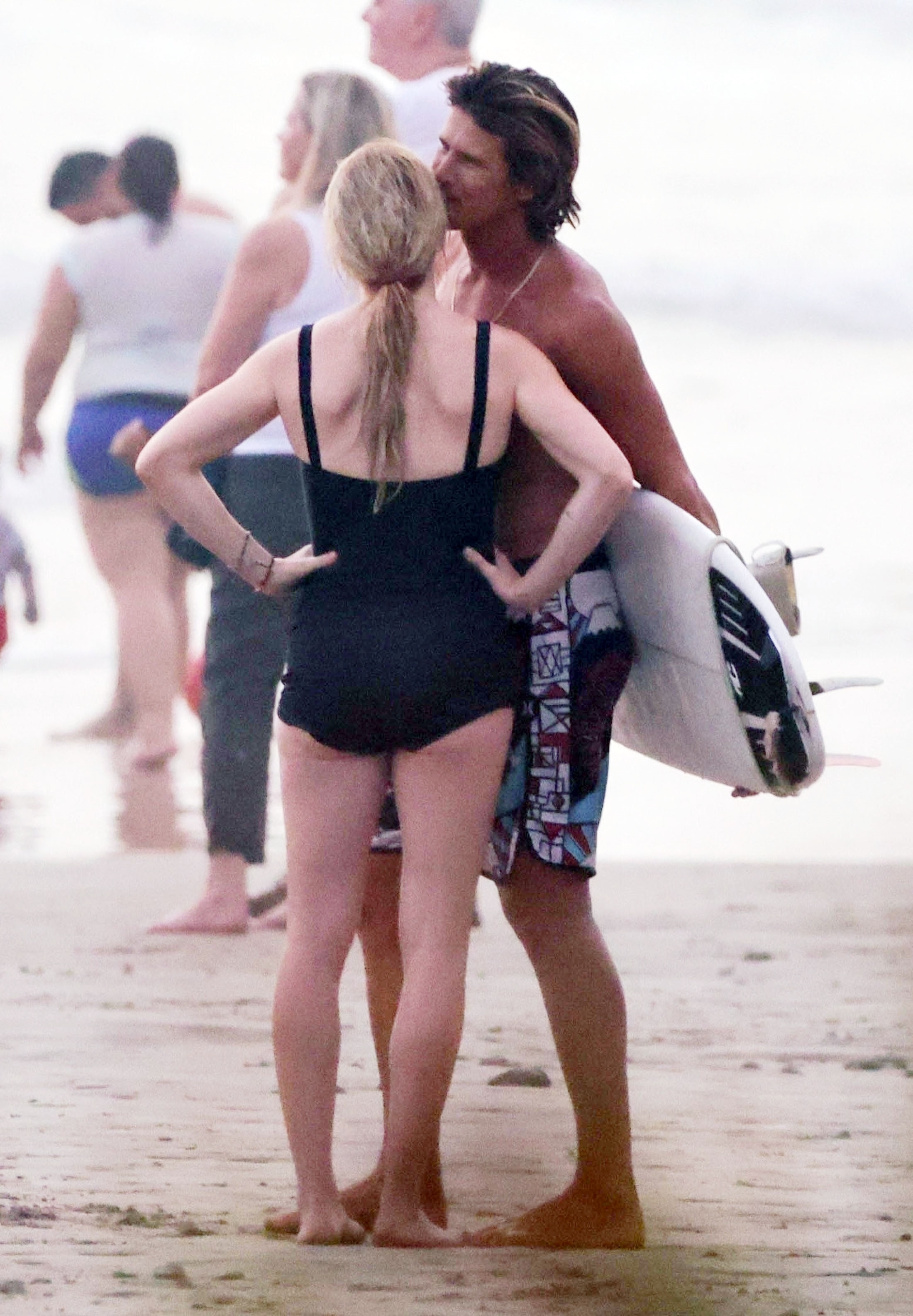Armando carried a surf board under his arm as he whispered in Ellie's ear