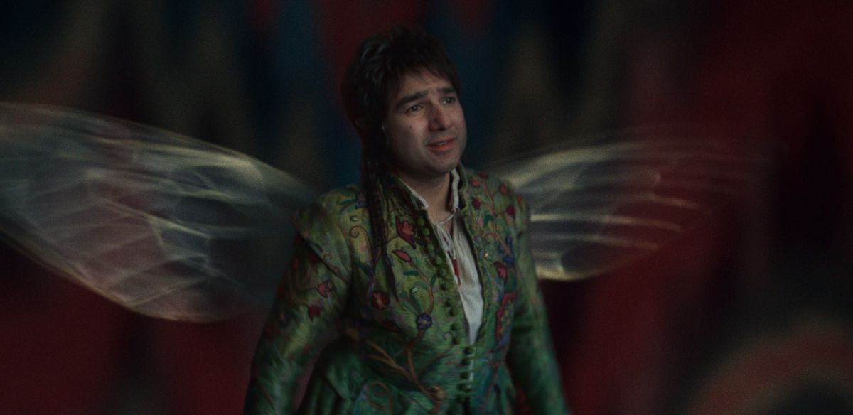 Nick Mohammed as Billy Blind, a man with fairy wings in an embroidered coat in Renegade Nell. 