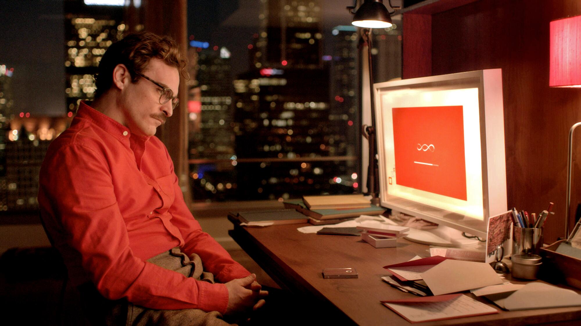 Joaquin Phoenix as Theodore in the movie "Her," sitting at computer desk. 