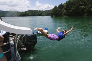 Child sliding off pontoon boat slide into lake on belly