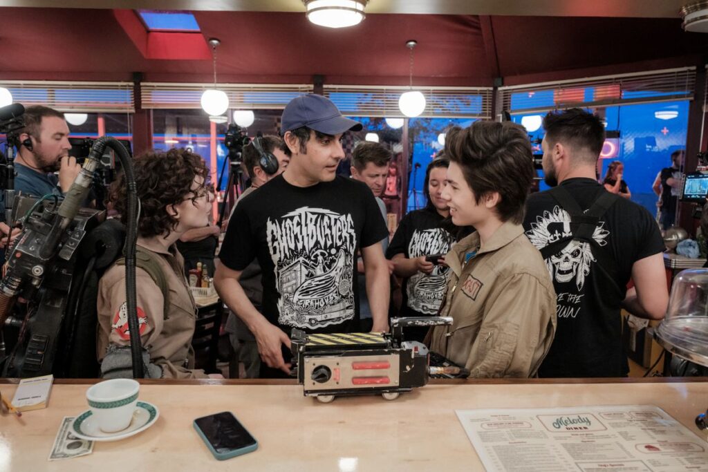 Director Gil Kenan talks to two teenagers in Ghostbusters uniforms in a diner set for Ghostbusters: Frozen Empire