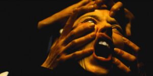 Cecilia (Sidney Sweeney) screams in an extreme close-up shot, as multiple sets of hands wrap around her face and indent her skin in Immaculate