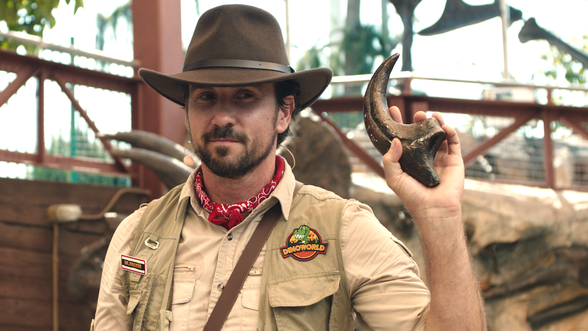 A man dressed like Dr. Grant from Jurassic Park holds a raptor claw in The Invisible Raptor